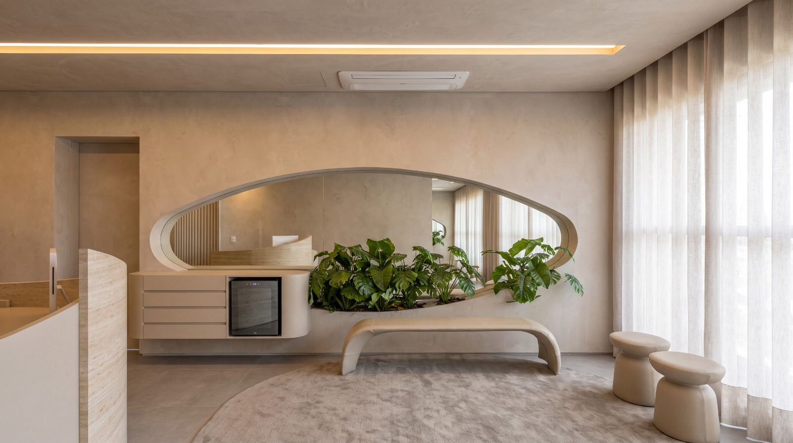 Lounge com espelho orgânico, banco curvo, plantas e cortinas de linho